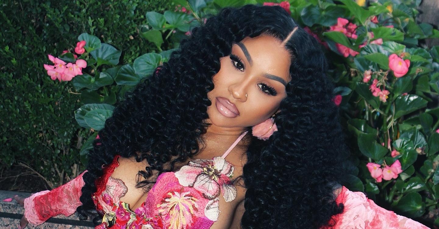 Ari Fletcher poses in front of pink flowers.